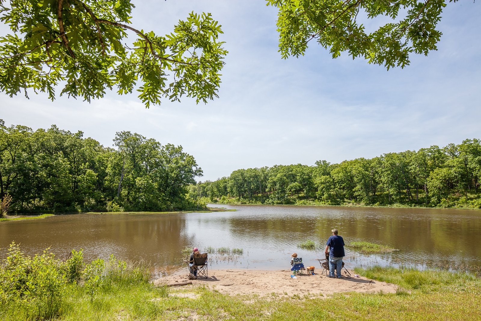 Visitors fishing beside a tree-lined lake at Knob Noster State Park